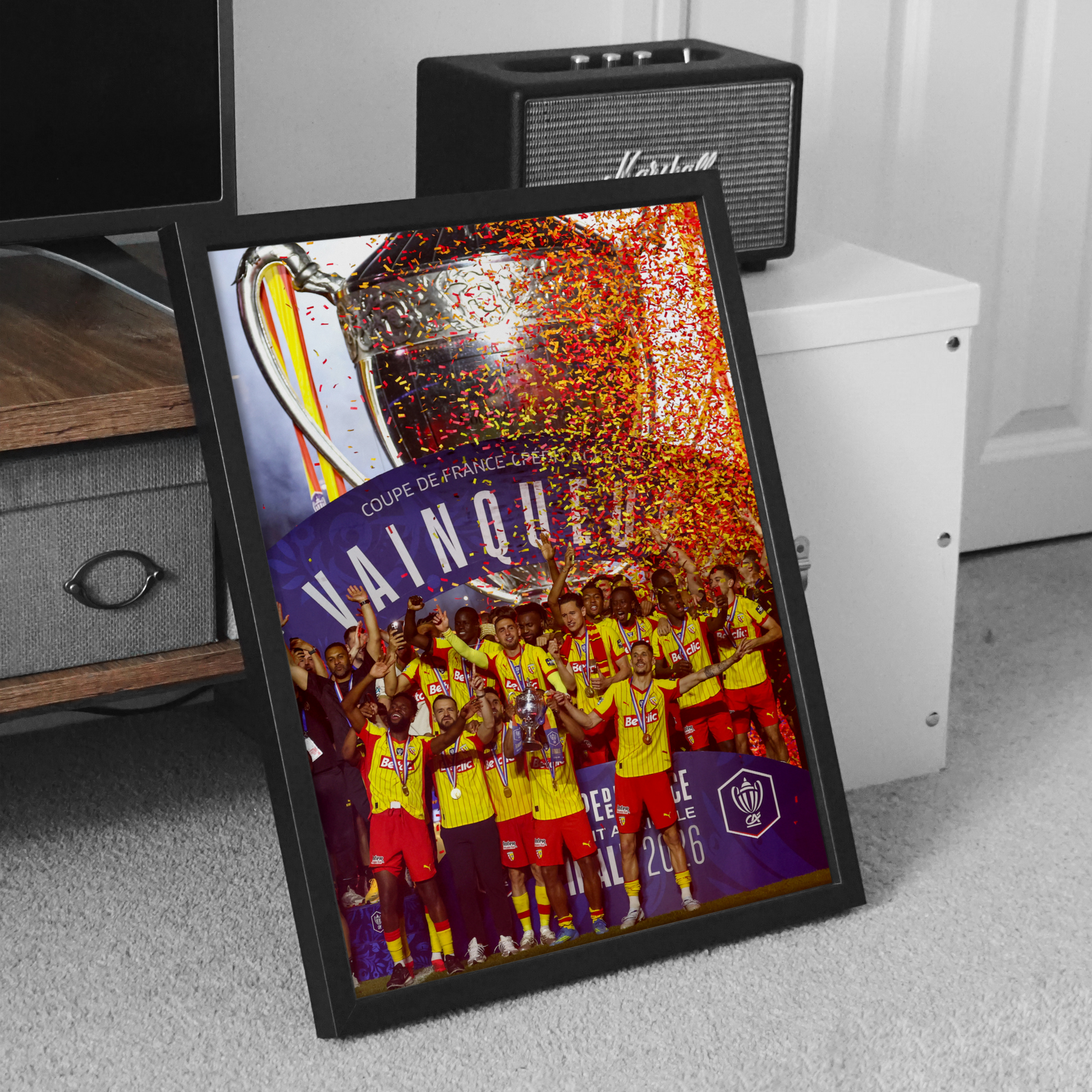 Cadre noir du RC Lens vainqueur de la Coupe de France 2026, posé au sol dans une décoration intérieure sobre en noir et blanc.