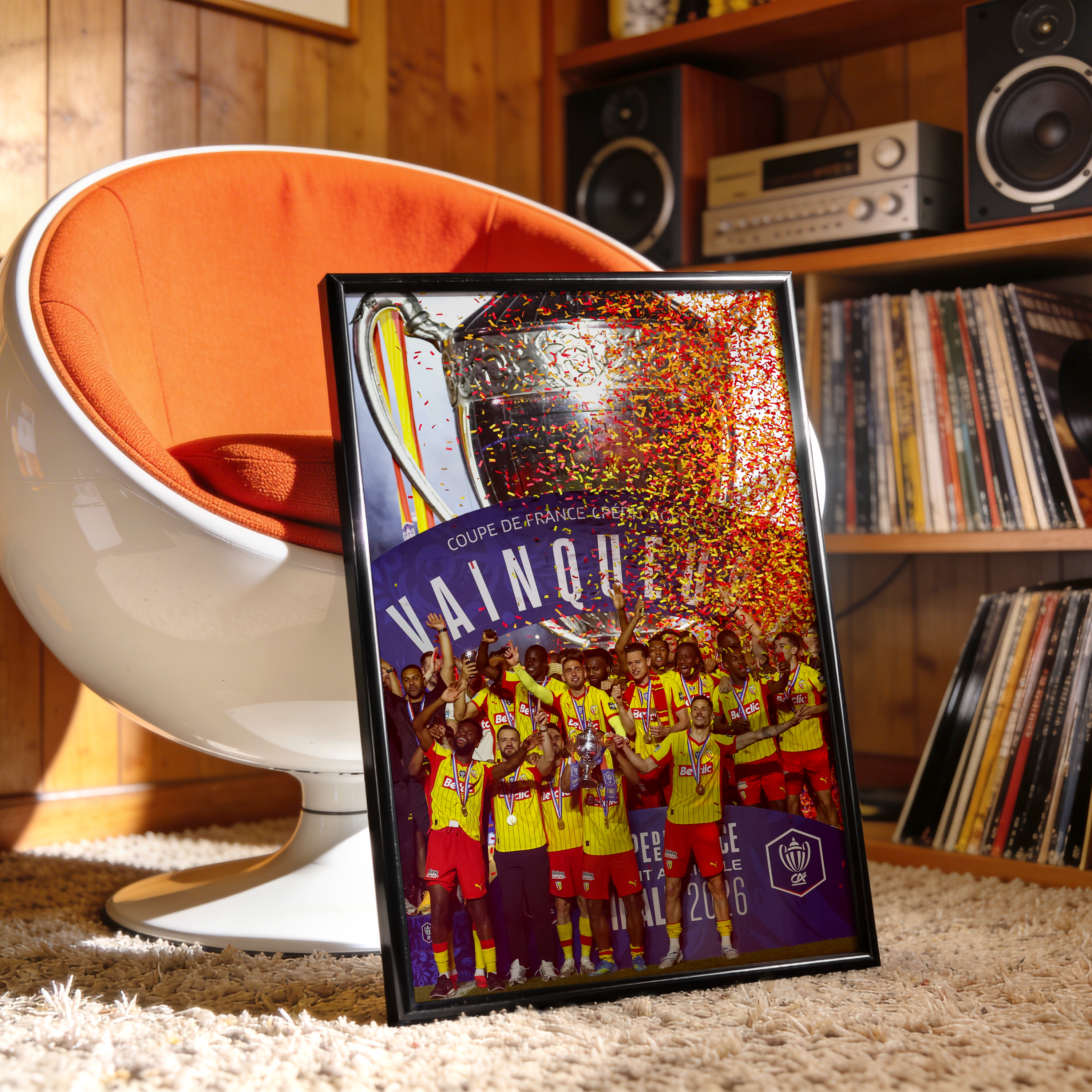 Affiche encadrée du RC Lens célébrant la Coupe de France 2026, posée dans un salon vintage avec fauteuil orange et vinyles en arrière-plan.