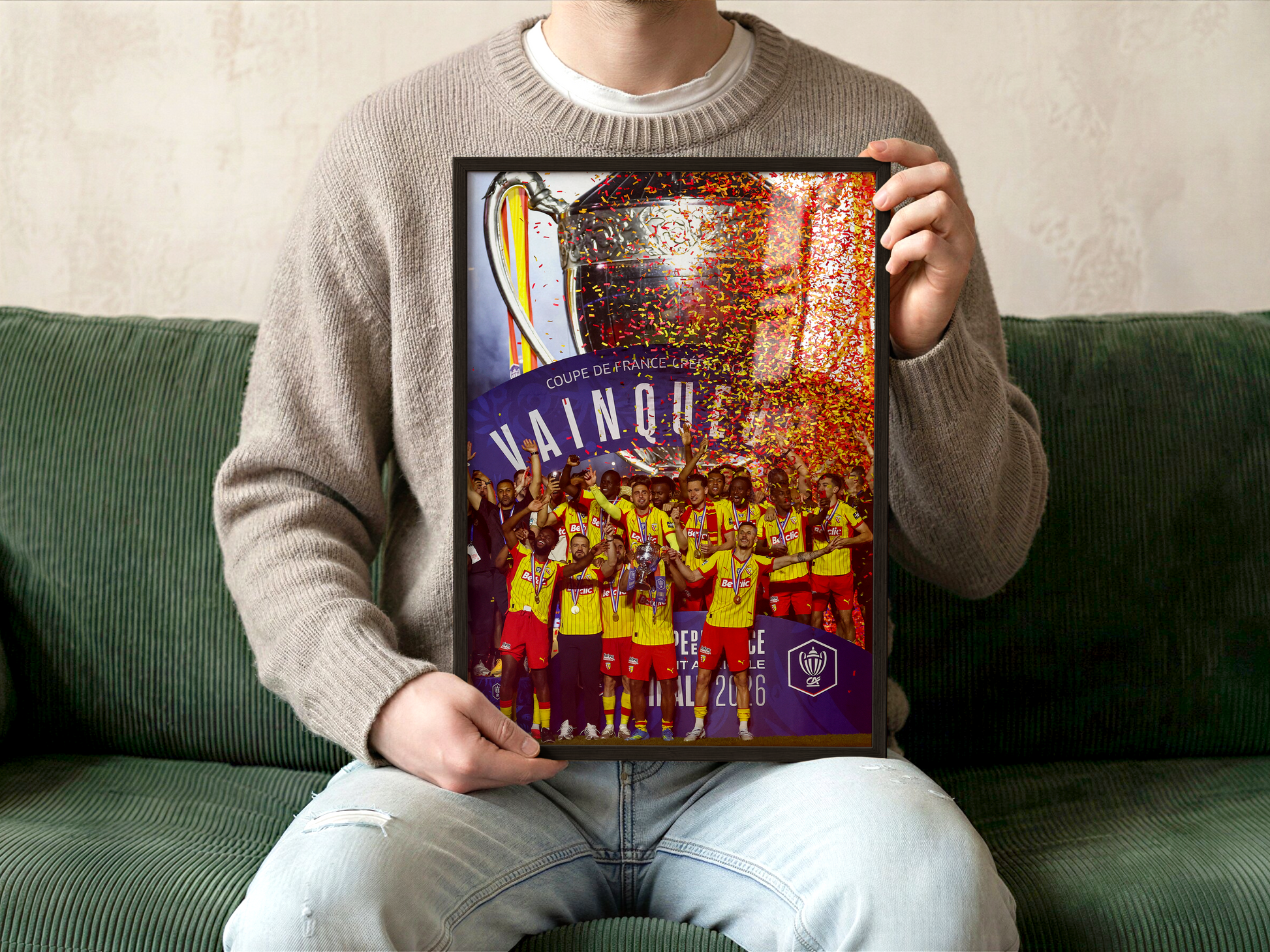 Personne tenant une affiche encadrée du RC Lens célébrant la victoire en Coupe de France 2026, avec les joueurs lensois et les confettis sang et or.